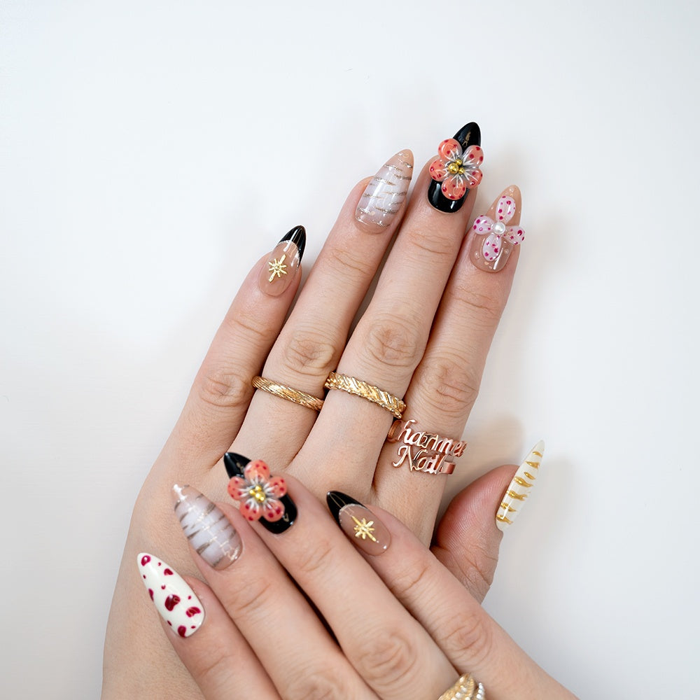 Elegant glossy nails in black, nude, and white with gold details and floral embellishments