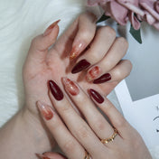 Chic burgundy almond nails featuring marble art and metallic gold accents