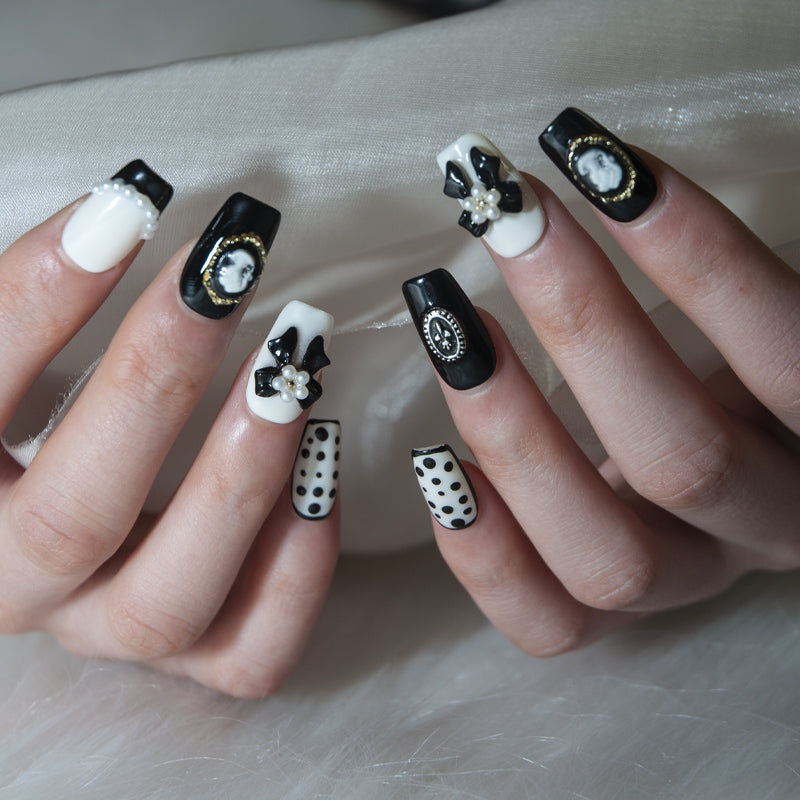Classy black and white nails with pearl accents, polka dots, and gold cameo frames