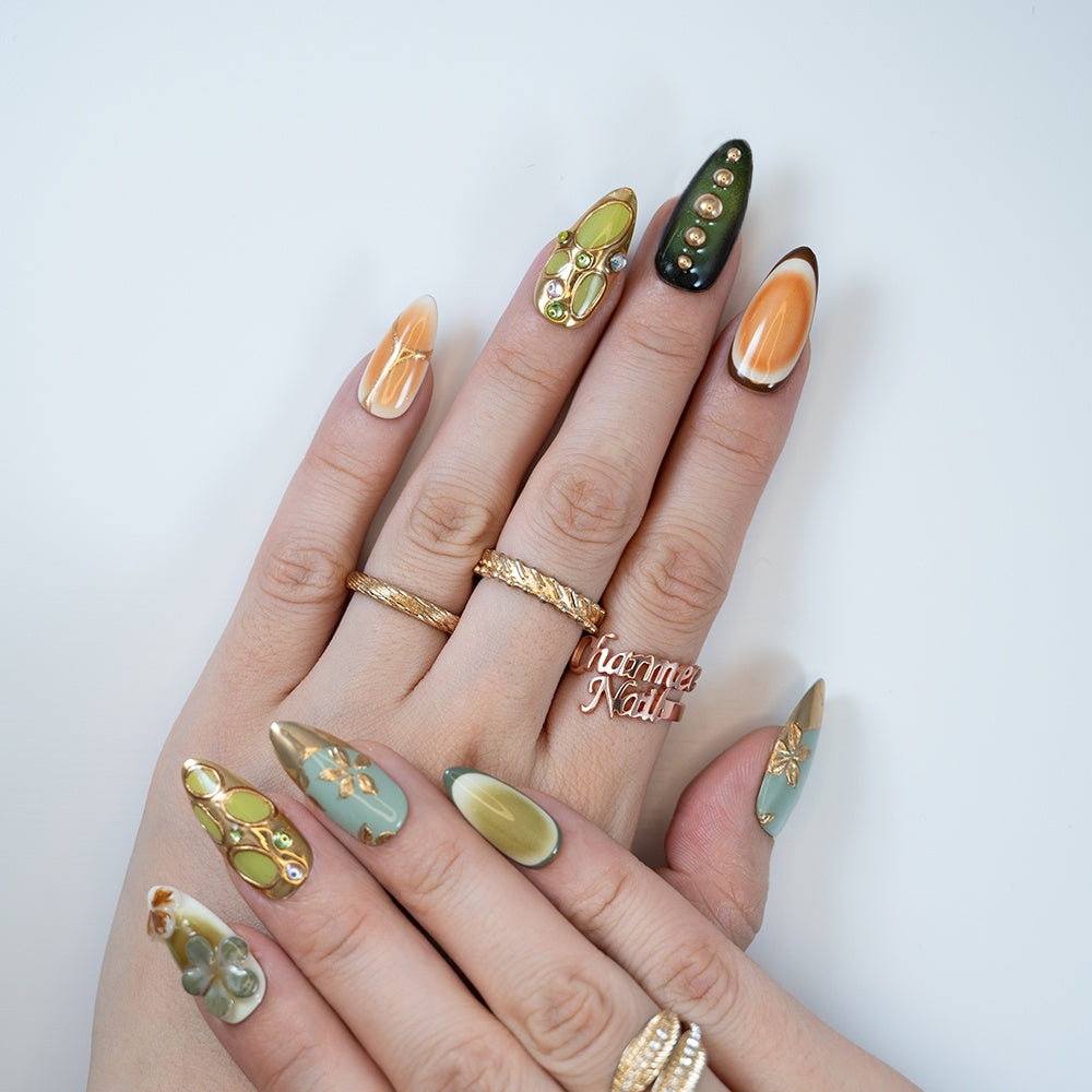 Green and gold press-on nails with metallic leaf patterns and gemstone accents