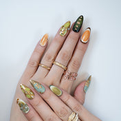 Green and gold press-on nails with metallic leaf patterns and gemstone accents