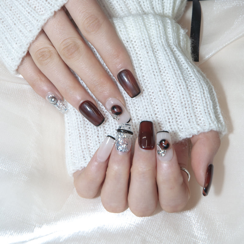 Glossy burgundy nails with silver glitter, pearl charms, and statement stones
