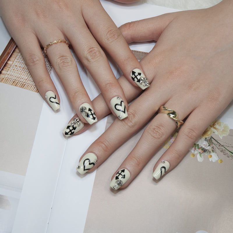 Handmade cream press-on nails with black motifs, rhinestones, and 3D metal charms