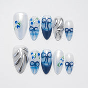 Medium blue and white press-on nails with hand-painted bows, silver accents, and berry designs