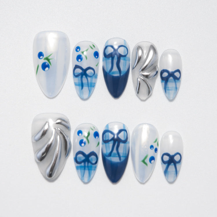 Medium blue and white press-on nails with hand-painted bows, silver accents, and berry designs