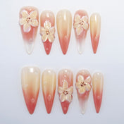 Long stiletto press-on nails with peach to nude ombre and 3D floral accents