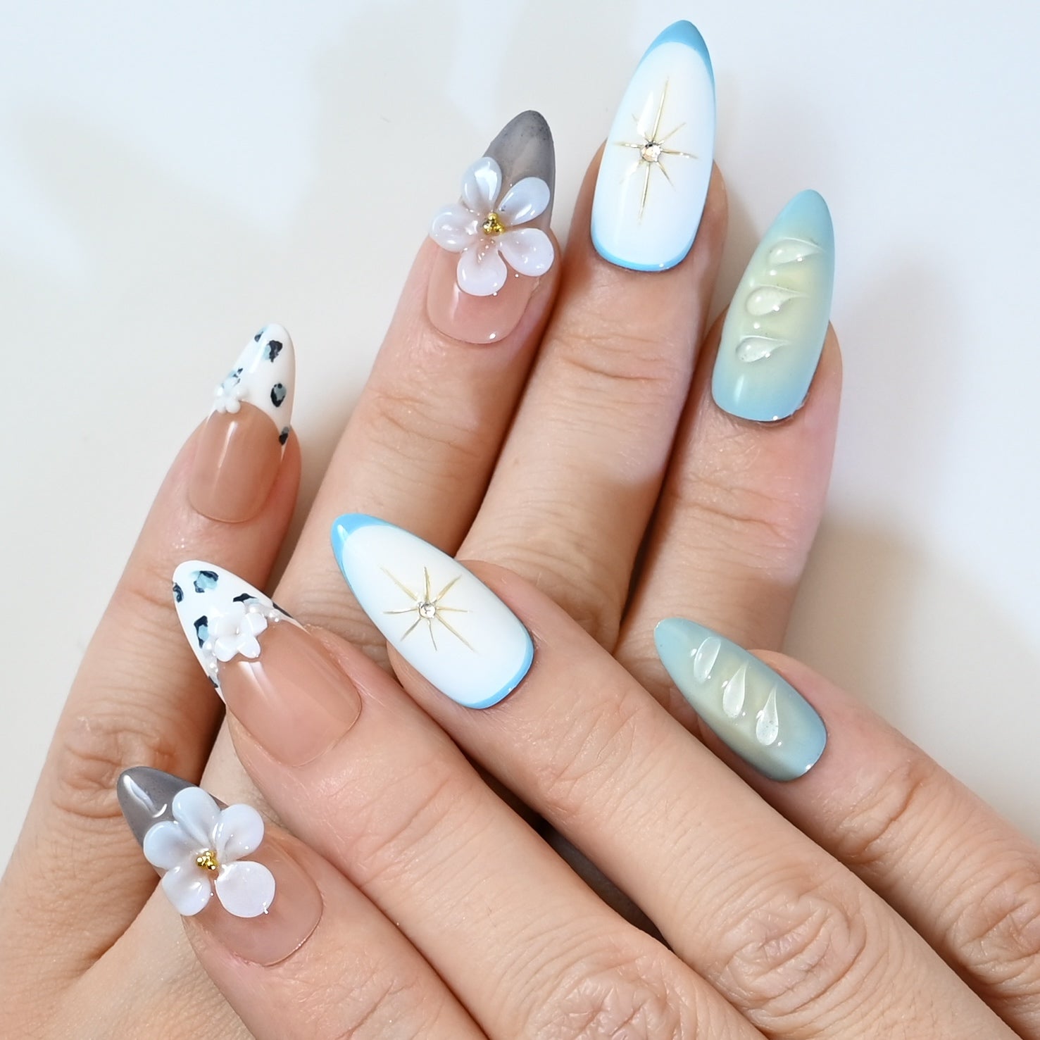 Chic press-on nails with soft nude base, grey floral art, and delicate gold bead embellishments