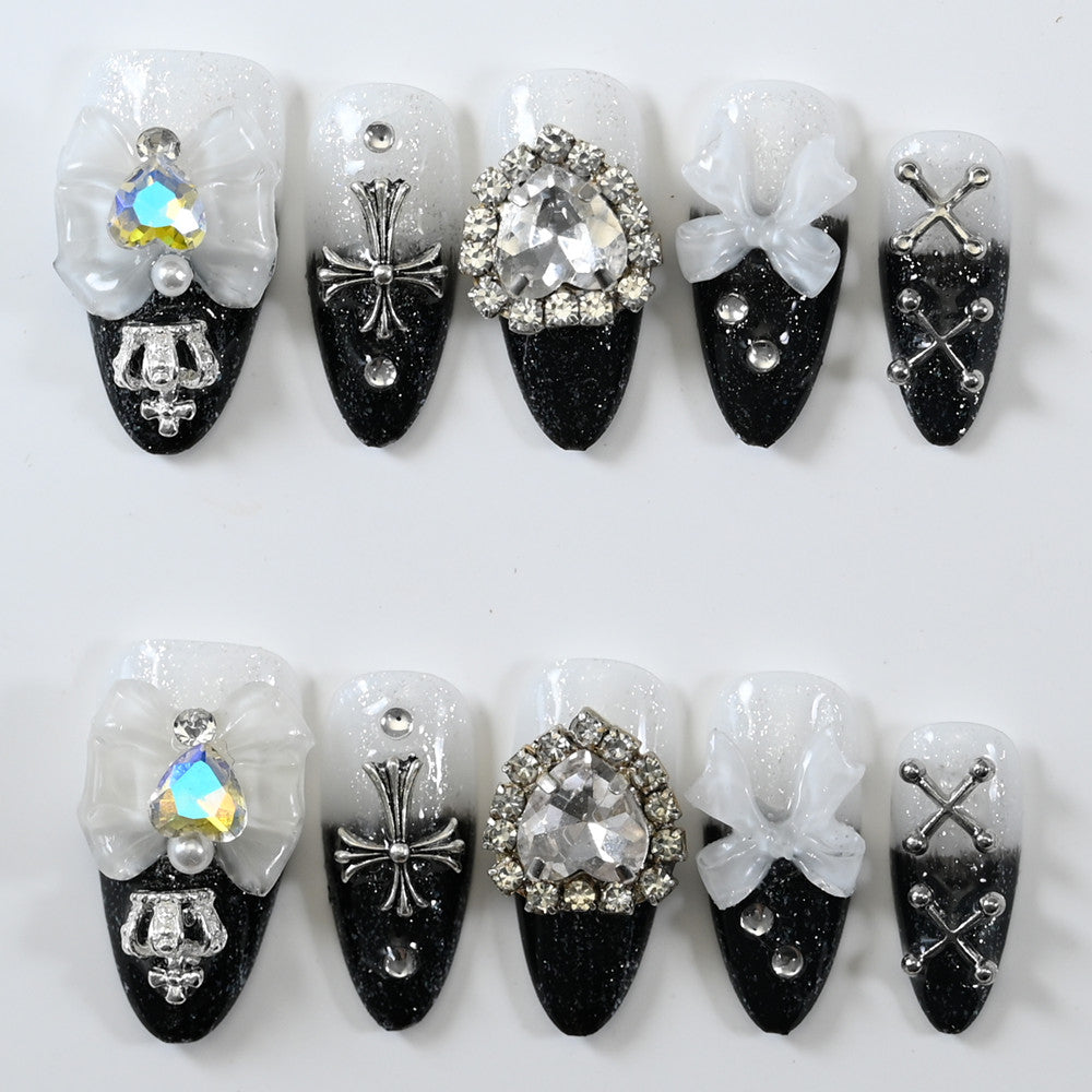 Black and white ombre press-on nails with 3D bows, rhinestone gems, and gothic cross charms