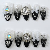 Black and white ombre press-on nails with 3D bows, rhinestone gems, and gothic cross charms