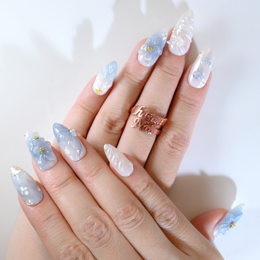 Elegant press-on nails in pastel blue with 3D blossoms, pearls, and butterfly charm