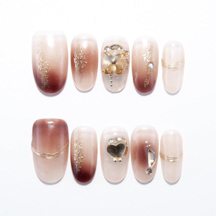 Brown to nude ombre press-on nails with gold leaf details and butterfly crystal charm
