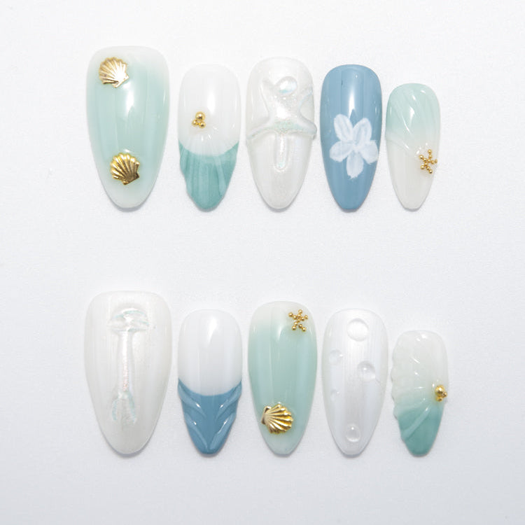 Beach-themed press-on nails with gold shell charms and sea green accents