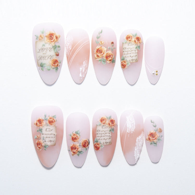 Almond press-on nails with vintage rose print, handwritten letter art, and nude pink base